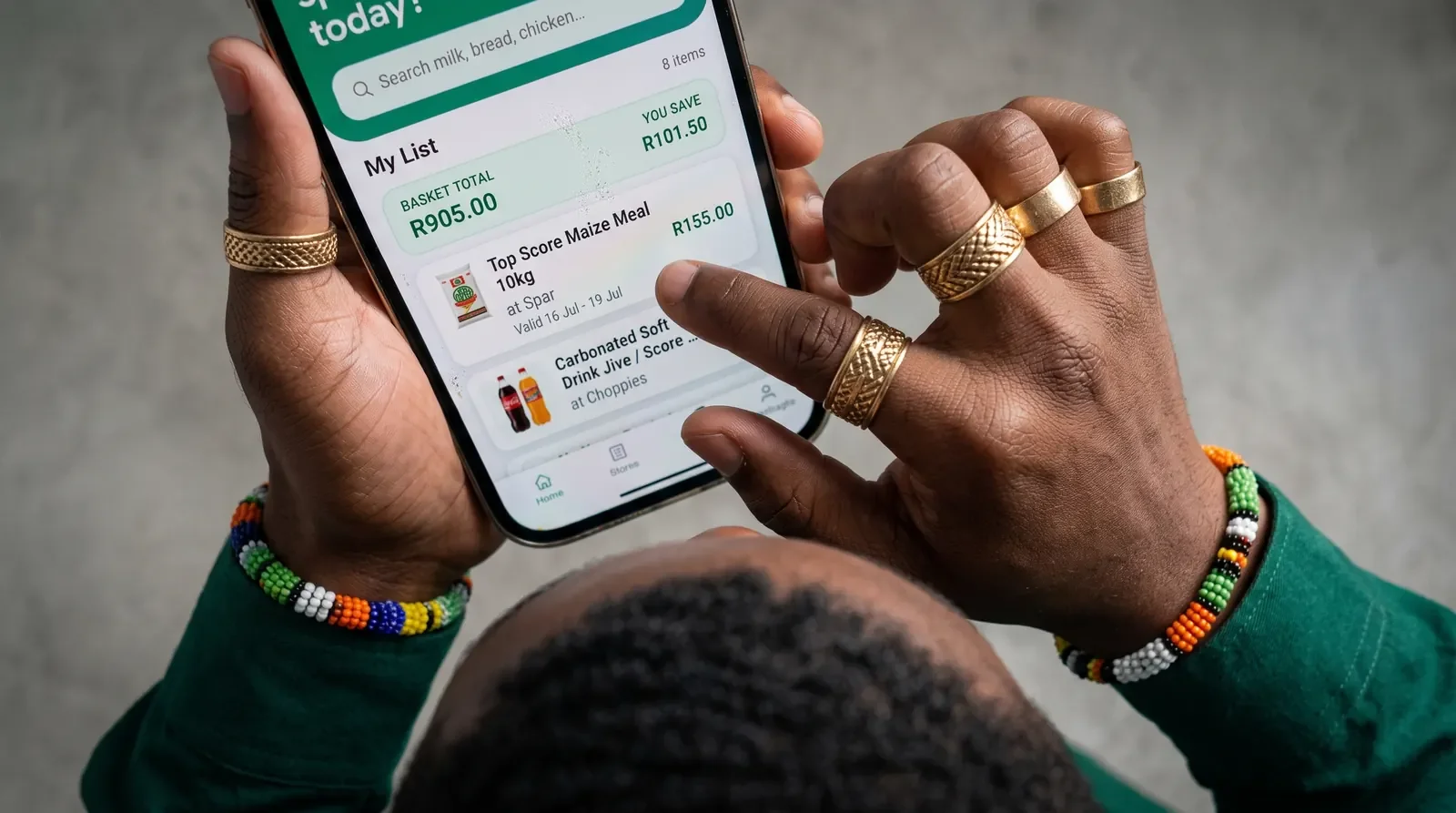 Two hands holding a phone showing a shopping list with a basket total and the amount saved