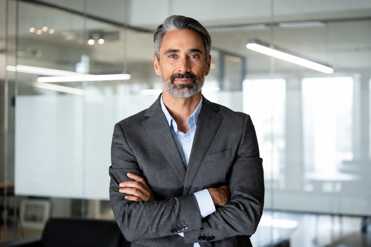 A managing director standing with arms folded in a glass-walled office.
