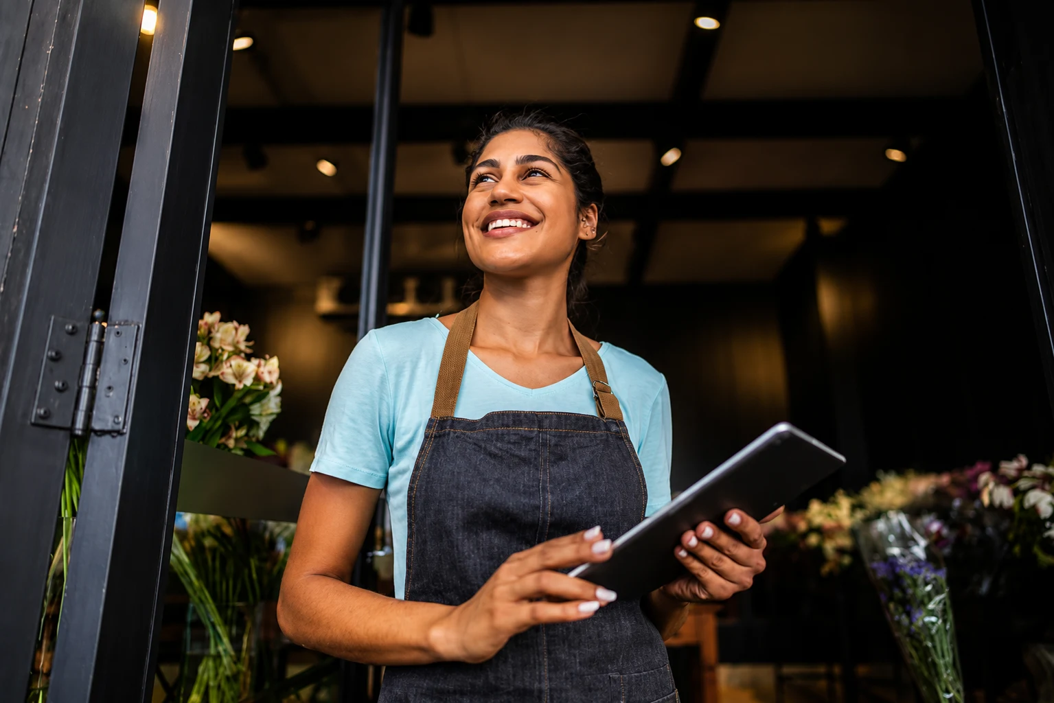 A florist holding a tablet in the doorway of her shop.