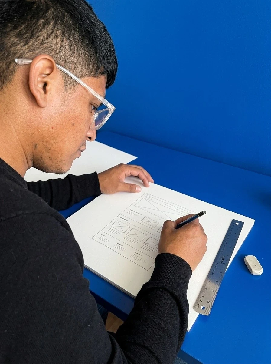Shaheed sketching a website wireframe in pencil at a cobalt desk